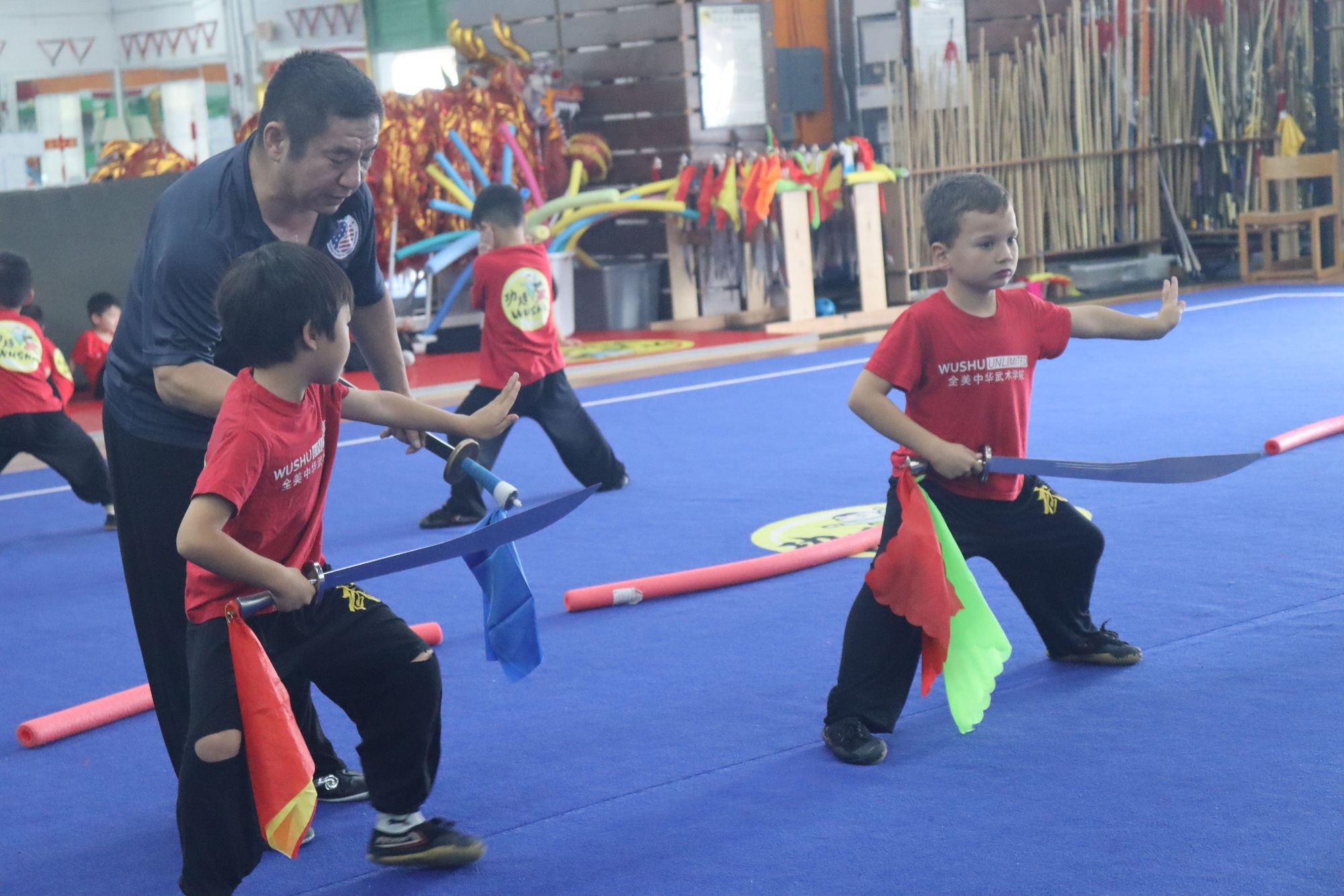 A coach guiding young students with silk flags at Wushu Unlimited