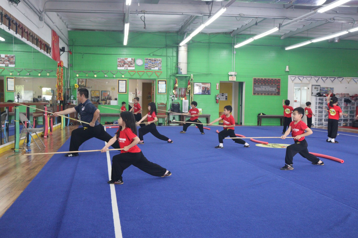 Children in bow stance with staffs across the training hall