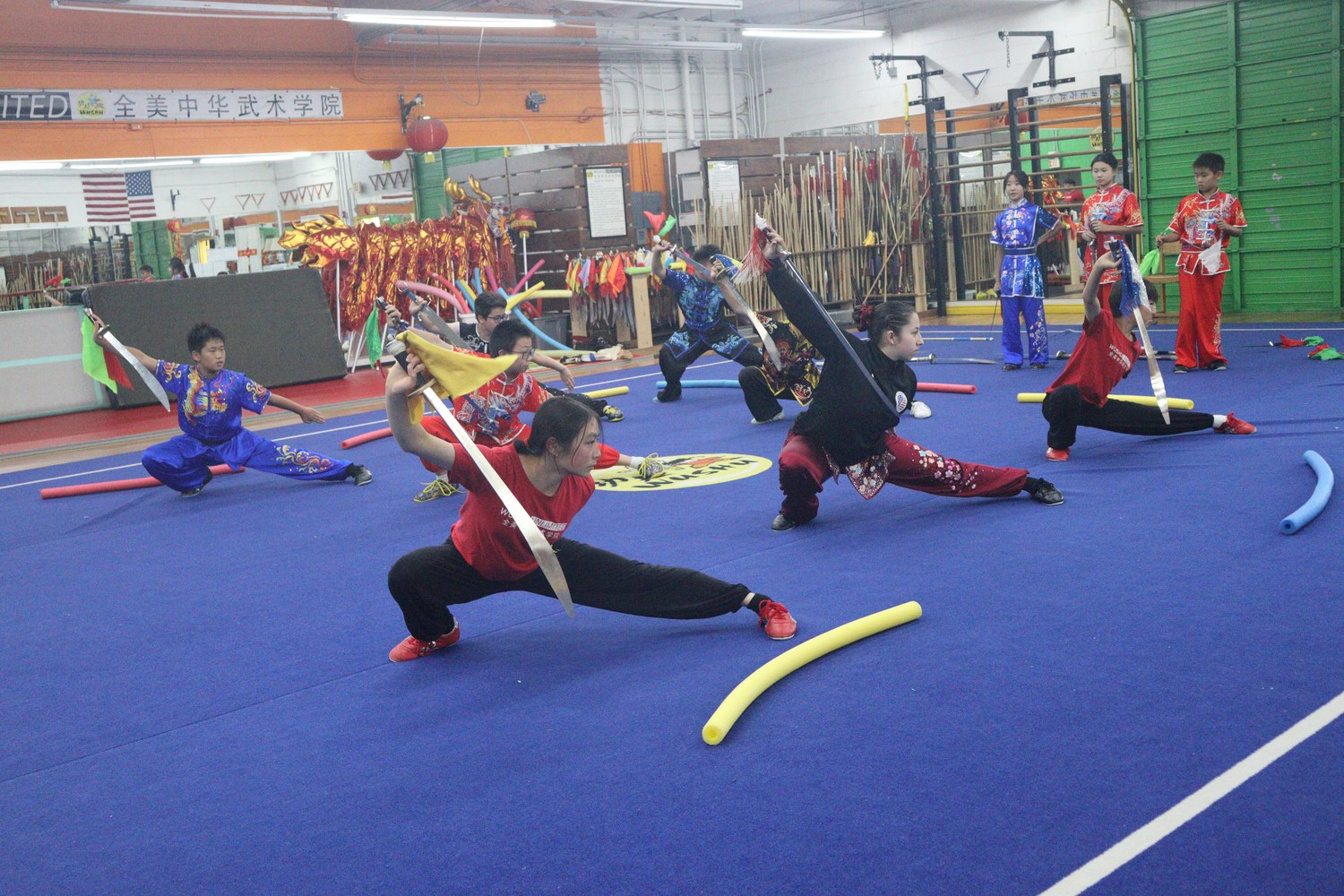 Class in competition silks holding deep stances with weapons